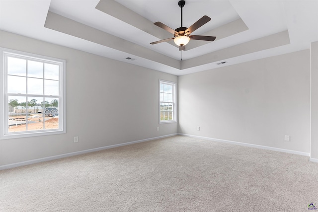 carpeted spare room with visible vents, a tray ceiling, and baseboards