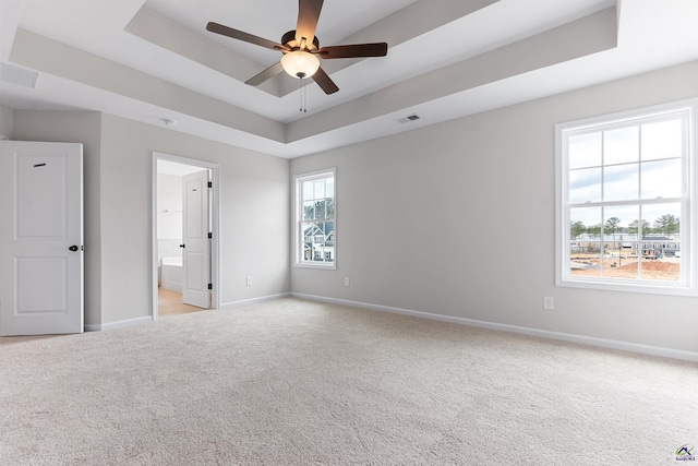 spare room with light carpet, a ceiling fan, visible vents, baseboards, and a tray ceiling