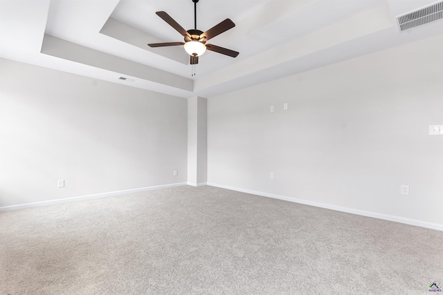 carpeted empty room featuring ceiling fan, a tray ceiling, visible vents, and baseboards