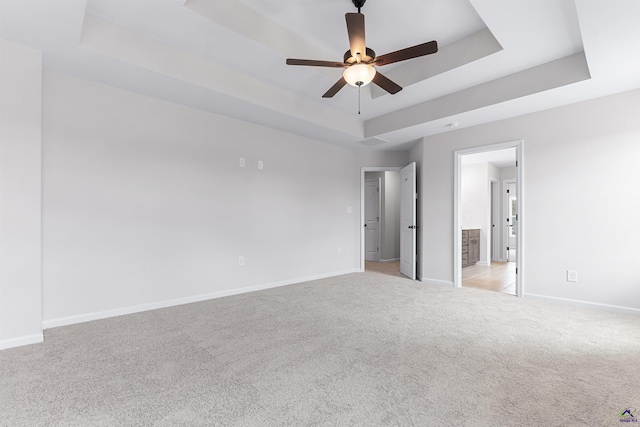 empty room featuring ceiling fan, light colored carpet, visible vents, baseboards, and a raised ceiling