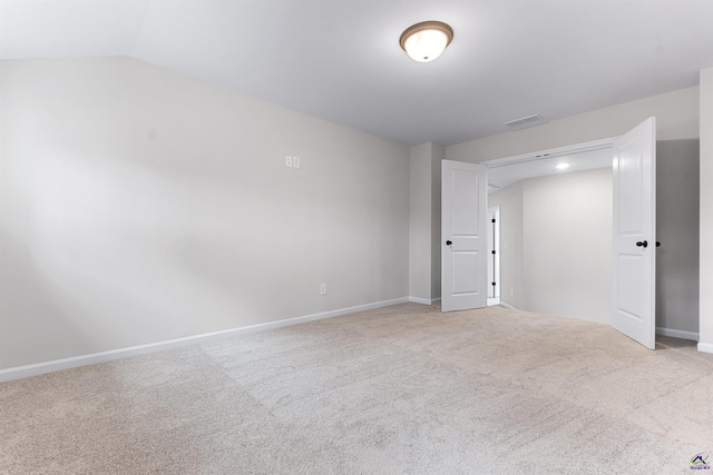 carpeted empty room featuring visible vents, vaulted ceiling, and baseboards