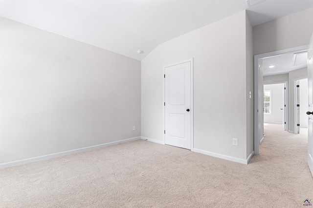 unfurnished bedroom featuring light carpet, vaulted ceiling, attic access, and baseboards