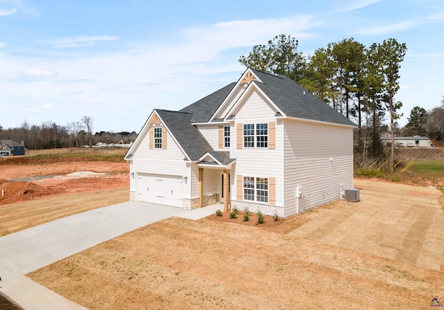 traditional home featuring central AC unit, a garage, driveway, stone siding, and roof with shingles