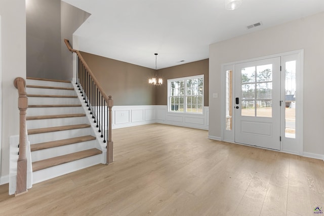 entrance foyer featuring a wainscoted wall, visible vents, stairway, wood finished floors, and a chandelier