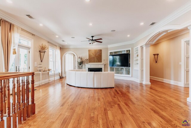 unfurnished living room featuring ornate columns, ornamental molding, built in features, light wood-type flooring, and ceiling fan