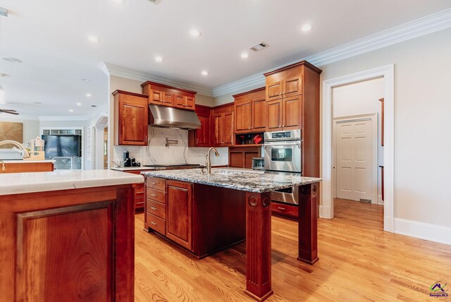 kitchen with stainless steel appliances, a center island with sink, ornamental molding, a breakfast bar, and light hardwood / wood-style floors