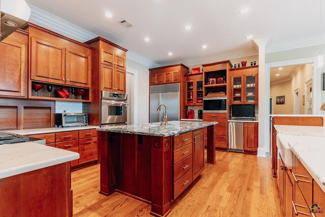 kitchen with a center island with sink, built in appliances, light hardwood / wood-style floors, crown molding, and light stone counters