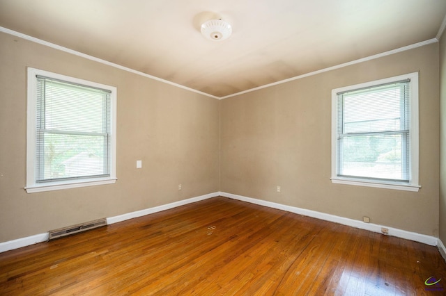 empty room featuring a wealth of natural light, ornamental molding, and wood-type flooring