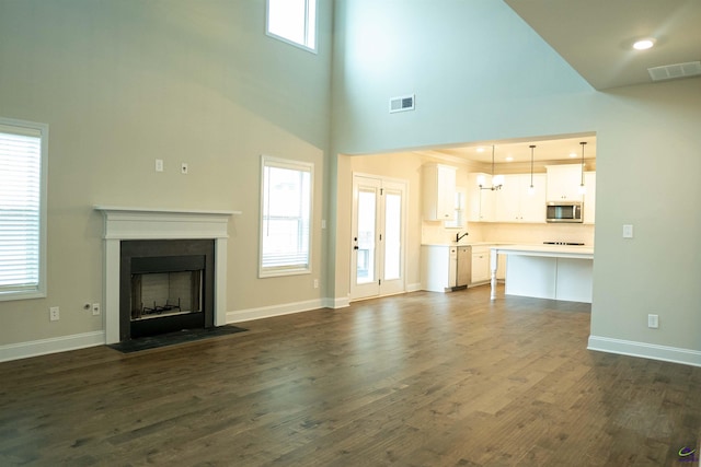 unfurnished living room featuring a towering ceiling, baseboards, dark wood-style floors, and visible vents