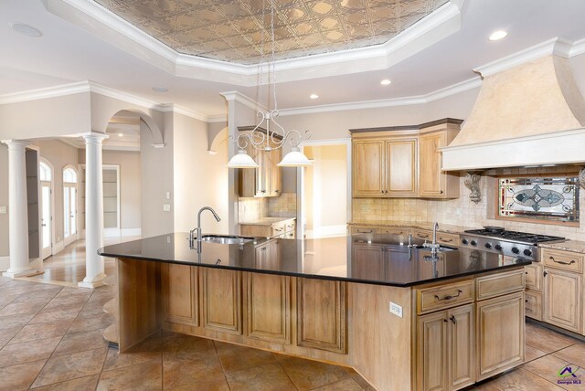 kitchen featuring stainless steel gas cooktop, ornamental molding, a tray ceiling, and an island with sink