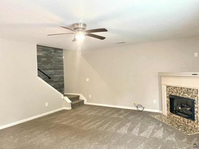 unfurnished living room with a tiled fireplace, carpet floors, a ceiling fan, and stairs