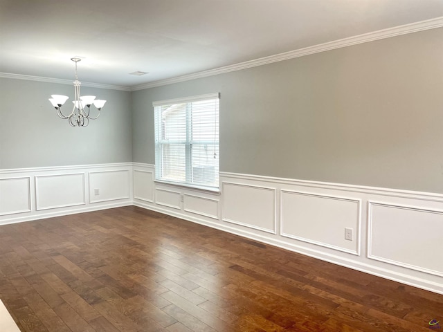 empty room featuring crown molding, wainscoting, dark wood finished floors, an inviting chandelier, and a decorative wall
