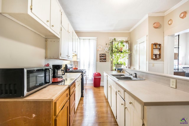 kitchen with appliances with stainless steel finishes, sink, white cabinets, ornamental molding, and light hardwood / wood-style flooring