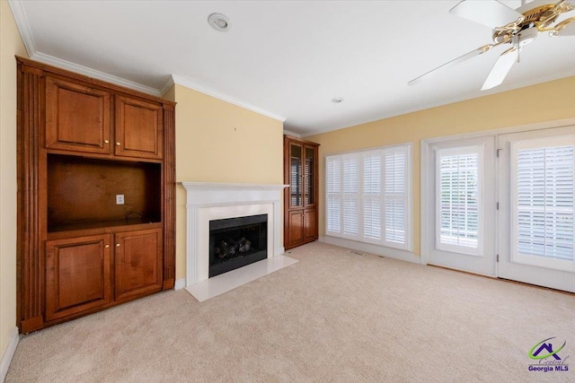 unfurnished living room with ceiling fan, ornamental molding, and light carpet