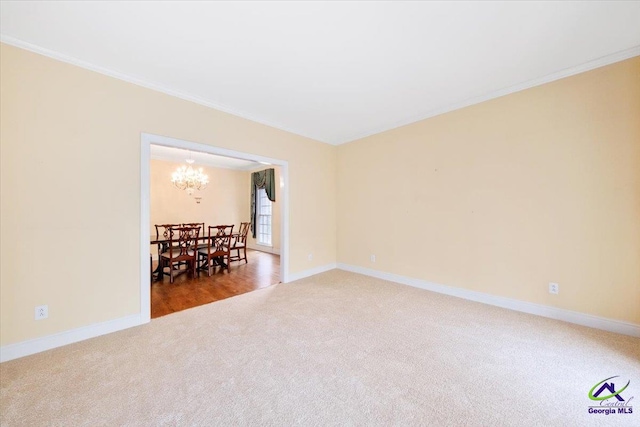 carpeted spare room with ornamental molding and an inviting chandelier