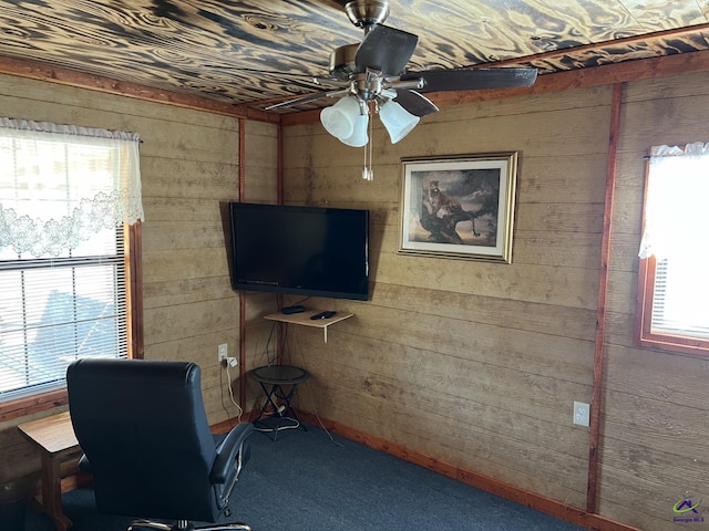 carpeted office space featuring wood walls and ceiling fan