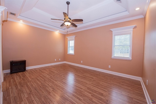 empty room featuring wood-type flooring, a tray ceiling, and ornamental molding