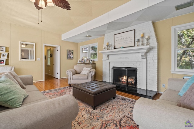 living room featuring wood-type flooring, a brick fireplace, ceiling fan, and a healthy amount of sunlight