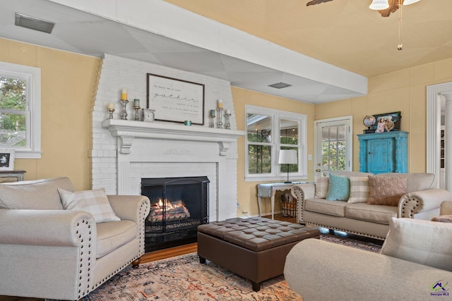 living room featuring hardwood / wood-style floors, ceiling fan, and a brick fireplace