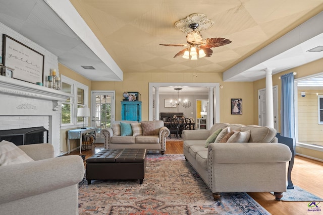 living room featuring a fireplace, ceiling fan with notable chandelier, hardwood / wood-style flooring, and decorative columns