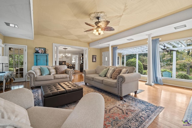 living room with hardwood / wood-style floors, ceiling fan with notable chandelier, vaulted ceiling, and decorative columns