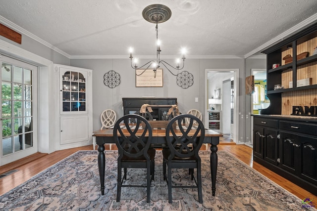 dining space with a textured ceiling, light wood-type flooring, crown molding, and a notable chandelier