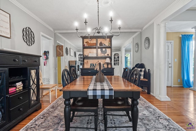 dining room with wood-type flooring, a textured ceiling, ornate columns, and ornamental molding