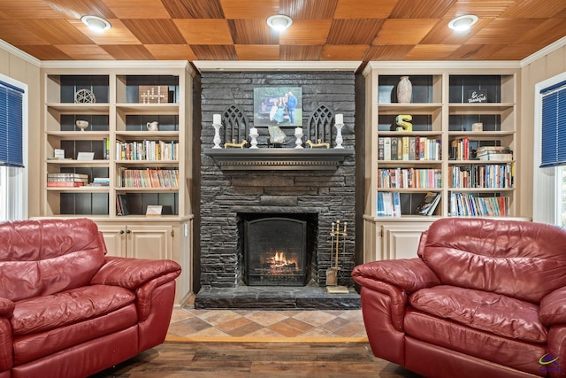 living area with a stone fireplace, built in features, and wood ceiling