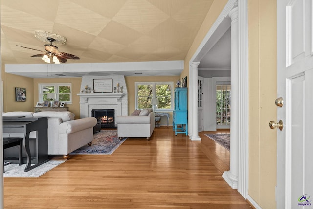 living room featuring hardwood / wood-style flooring, ceiling fan, ornate columns, and a brick fireplace