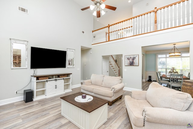 living room featuring a high ceiling, light hardwood / wood-style floors, and ceiling fan with notable chandelier