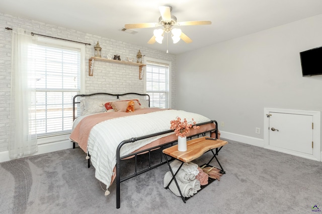 bedroom featuring multiple windows, carpet, ceiling fan, and brick wall