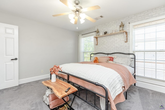 carpeted bedroom with brick wall, multiple windows, and ceiling fan