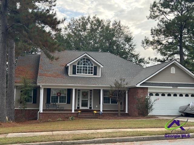 cape cod home with covered porch, driveway, a front yard, and a garage