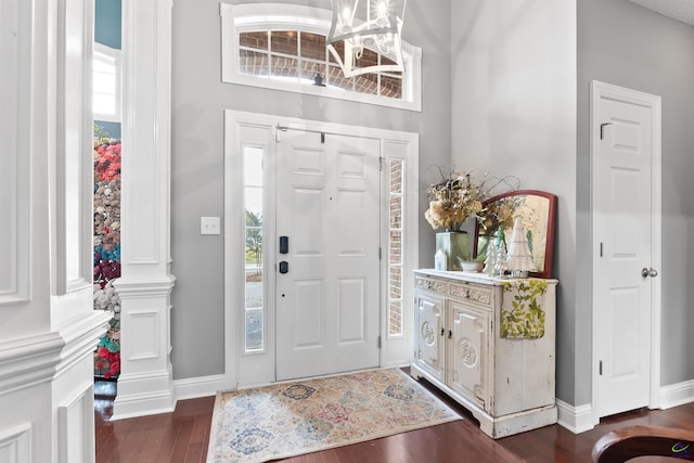 foyer featuring dark hardwood / wood-style flooring, decorative columns, and a notable chandelier