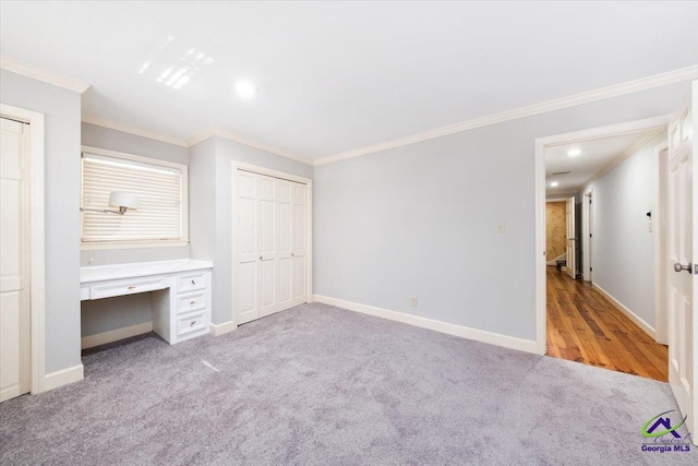 unfurnished bedroom with built in desk, light colored carpet, a closet, and crown molding