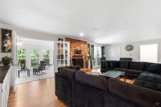 living room with a brick fireplace, light hardwood / wood-style flooring, ceiling fan, and ornamental molding