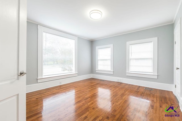 spare room featuring hardwood / wood-style floors, a healthy amount of sunlight, and crown molding