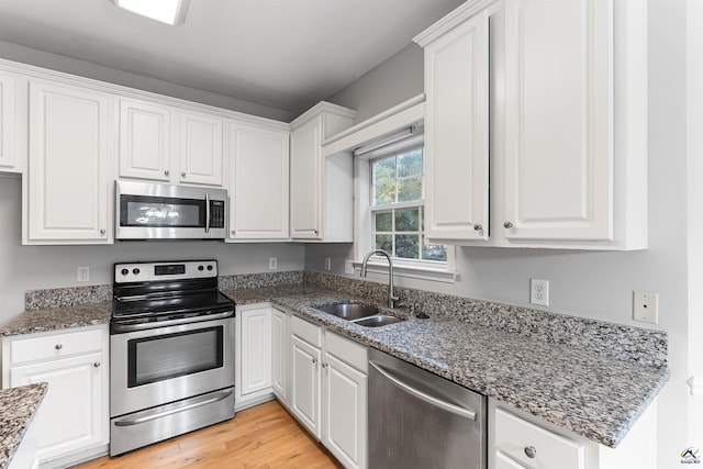 kitchen with dark stone counters, white cabinets, sink, light wood-type flooring, and appliances with stainless steel finishes