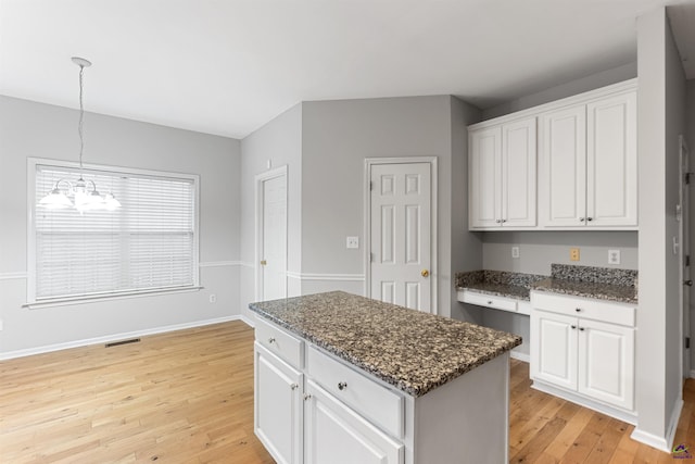 kitchen with white cabinetry, a center island, an inviting chandelier, light hardwood / wood-style floors, and built in desk