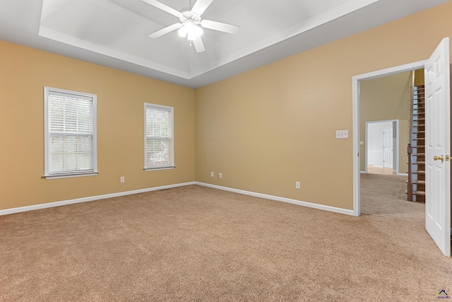 carpeted spare room with a raised ceiling and ceiling fan