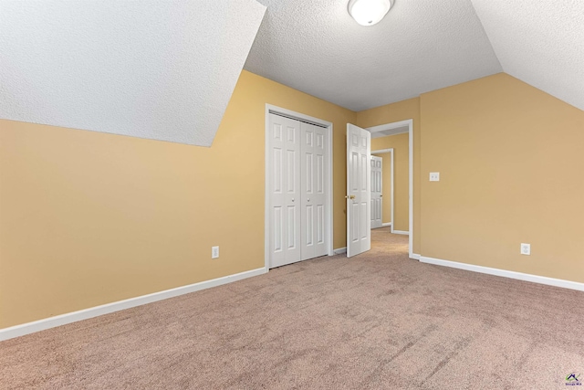 unfurnished bedroom featuring a textured ceiling, carpet floors, vaulted ceiling, and a closet