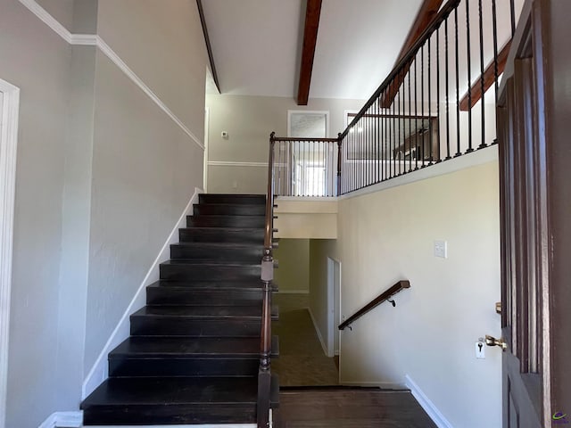 stairs featuring a towering ceiling, beamed ceiling, and wood-type flooring