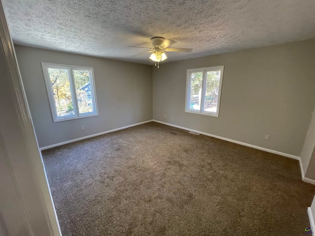 spare room featuring dark colored carpet, a textured ceiling, and plenty of natural light