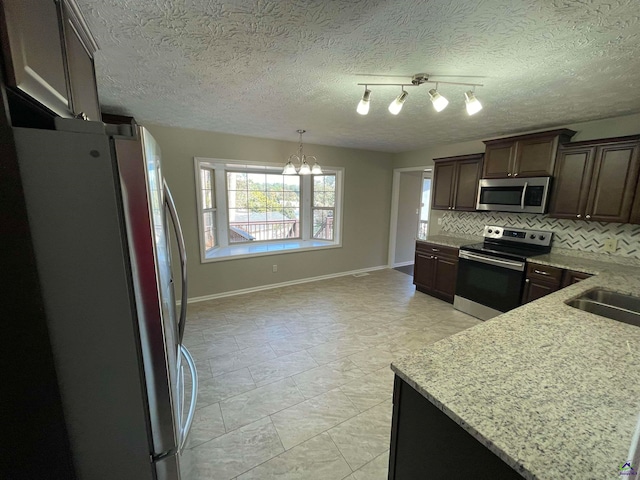 kitchen featuring a textured ceiling, light stone countertops, backsplash, and appliances with stainless steel finishes