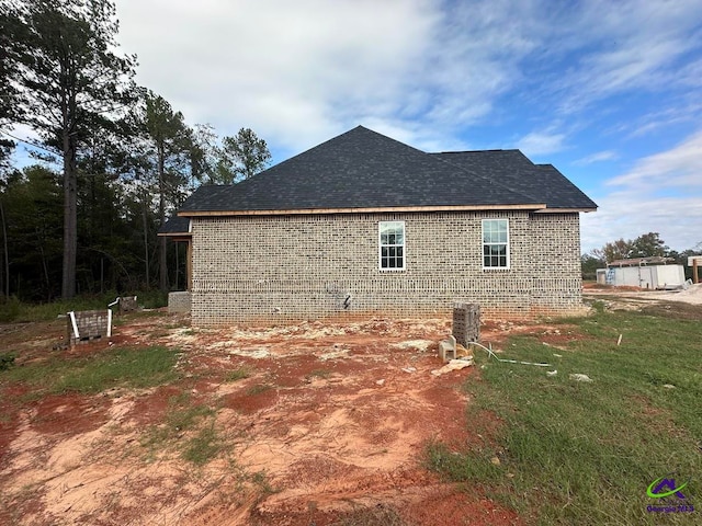 view of side of property featuring a shingled roof and brick siding