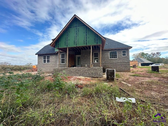 back of house with roof with shingles, a porch, and brick siding