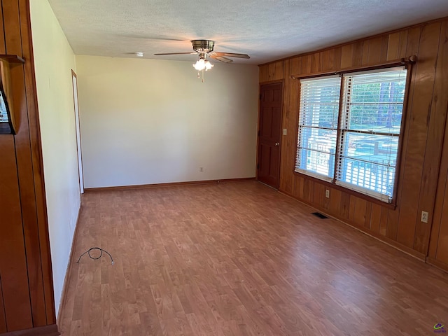 spare room featuring a textured ceiling, light hardwood / wood-style floors, ceiling fan, and wooden walls