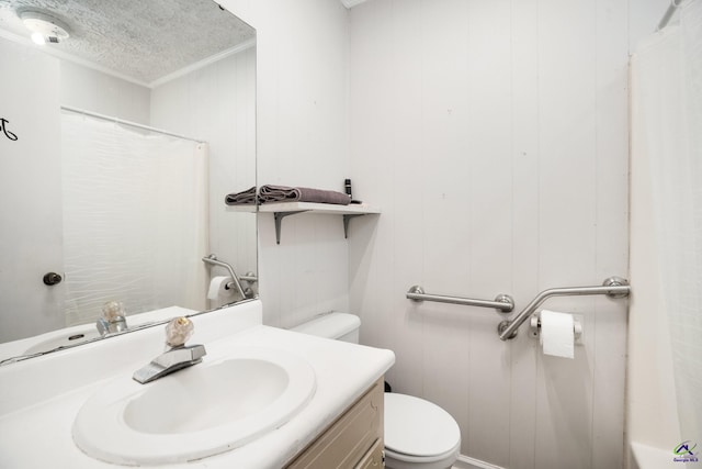 bathroom with a textured ceiling, toilet, wooden walls, vanity, and ornamental molding