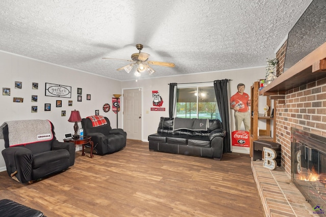 living room with ceiling fan, hardwood / wood-style floors, a textured ceiling, and a brick fireplace