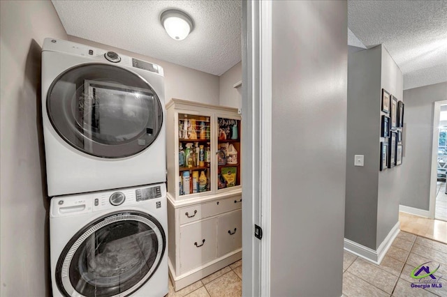 laundry room with light tile patterned floors, stacked washing maching and dryer, and a textured ceiling